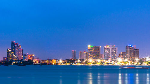 Illuminated cityscape by sea against clear blue sky at twilight