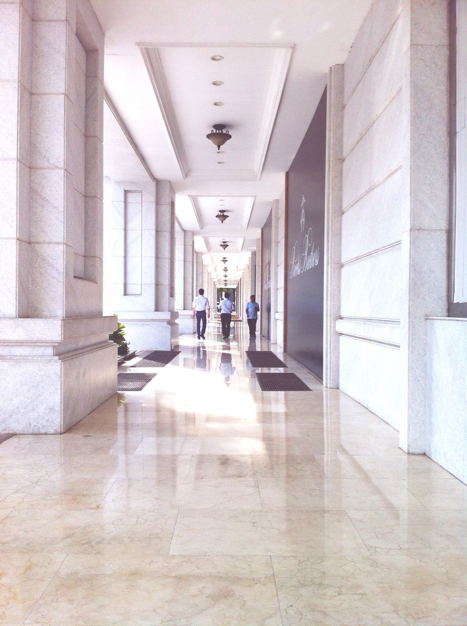 indoors, architecture, corridor, built structure, tiled floor, flooring, ceiling, empty, architectural column, the way forward, lighting equipment, in a row, building, modern, tile, wall - building feature, absence, reflection, illuminated, diminishing perspective