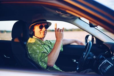 Portrait of smiling mature man gesturing while sitting in car