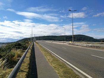 Country road leading towards mountain against sky