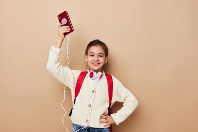 Portrait of girl holding smart phone against beige background