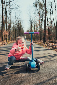 Full length of cute girl crouching on scooter in forest