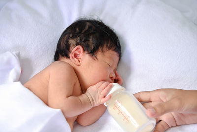 Cropped hand of mother feeding milk to daughter sleeping on bed at home