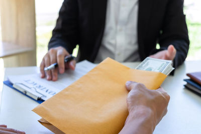 Cropped hand of person holding bribe by businessman on table