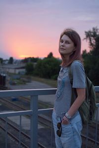 Portrait of young woman looking away while standing against railing