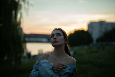 Young woman looking away while standing outdoors during sunset