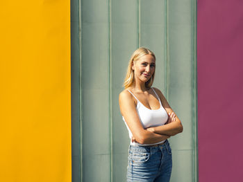 Portrait of smiling young woman standing against wall