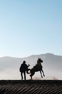 Silhouette man with horse at desert against clear sky