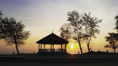 Silhouette gazebo by tree against sky during sunset