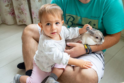 Infant baby girl playing with decorative rabbit in father s hands