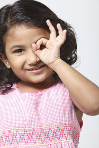 Portrait of girl shaping sunglasses with fingers over white background