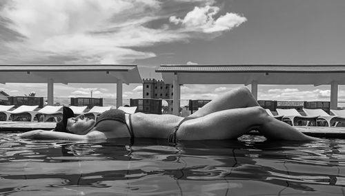 Side view of woman sitting on lounge chair against sky