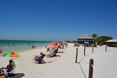 Group of people on beach against clear blue sky