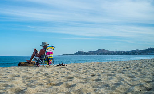 Person sitting on armchair at beach against sky