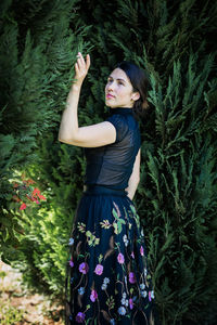 A young pretty woman in black clothes is standing near a bush