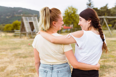 Rear view of girlfriends with arms around standing on field