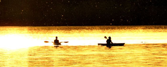 Silhouette men on lake against sky during sunset