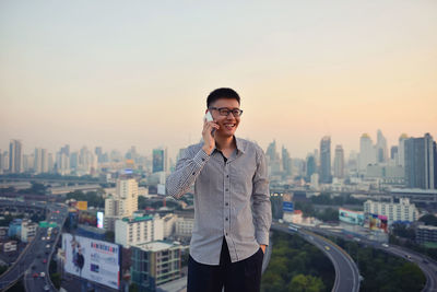 Businessman talking while standing against cityscape during sunset