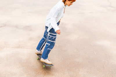 From above side view of active female in casual wear riding skateboard in skate park with ramp on summer day
