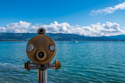 Close-up of coin-operated binoculars by sea against sky