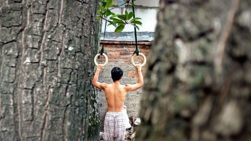 Rear view of shirtless man holding gymnastic rings