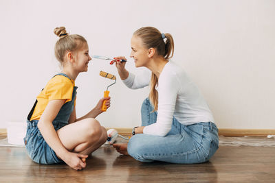 Beautiful and happy mom and daughter paint the walls in the apartment white, laugh and indulge.