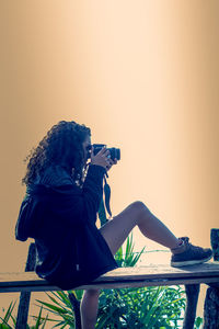 Side view of woman photographing on railing against sky