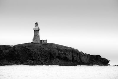 Lighthouse on cliff by sea against clear sky
