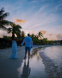 Rear view of women standing by palm trees against sky