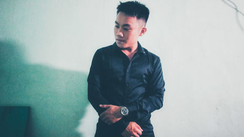 Young man looking away while standing against wall
