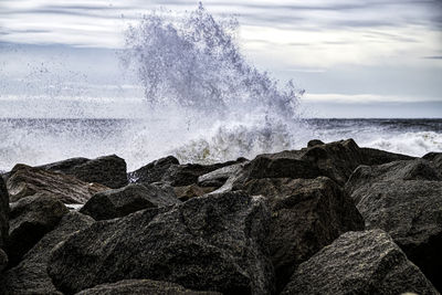 Waves splashing on rocks at shore against sky