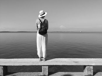 Rear view of woman standing on retaining wall against sea and sky
