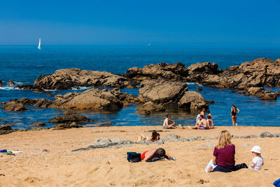 People sitting on rocks by sea against clear sky