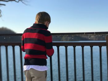 Rear view of boy standing by railing against clear sky