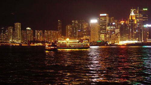 Illuminated buildings by sea against sky at night