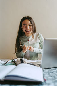 Portrait of cheerful young woman doing homework at table