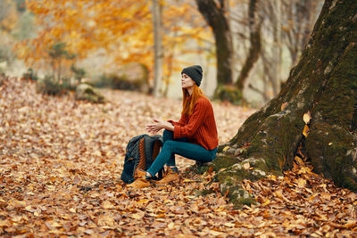 Side view of young woman sitting on ground during autumn