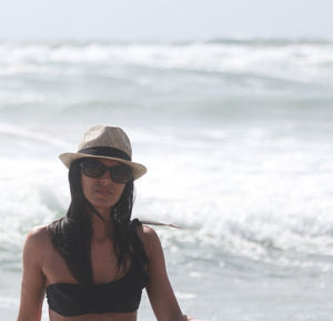 Portrait of woman wearing sunglasses and hat standing at beach during summer
