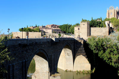 Arch bridge over river by buildings against clear sky