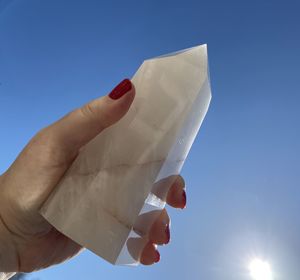 Female holding clear quartz crystal against blue sky