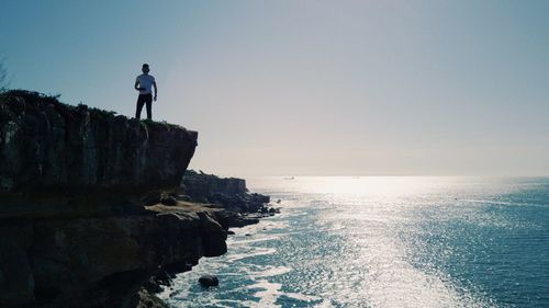 Rear view of man standing on rock by sea against sky