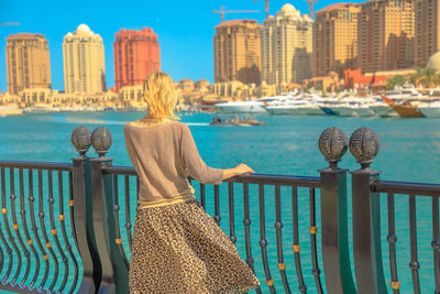 Rear view of woman looking at sea against cityscape