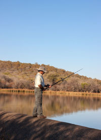 Man fishing in lake against clear sky