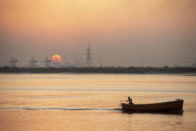 Man on boat in river against sky during sunset