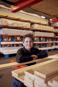 Portrait of smiling mature female worker leaning on plank at lumber industry