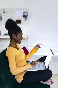 Smiling afro woman using laptop for online shopping in living room at home