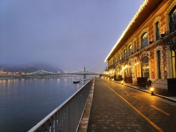 Illuminated buildings by river against sky at dusk
