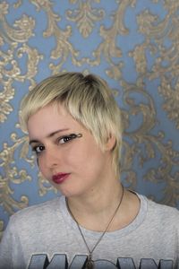 Portrait of young woman with short blond hair against patterned wall
