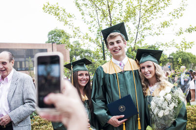 Cropped image of person photographing graduate students at graduation ceremony person