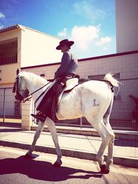 Woman riding horse in ranch against sky